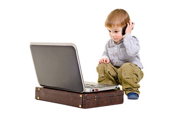 Small boy talking on smartphone while looking at laptop computer.